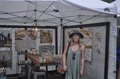 a woman standing in front of a white tent with paintings on the wall behind it