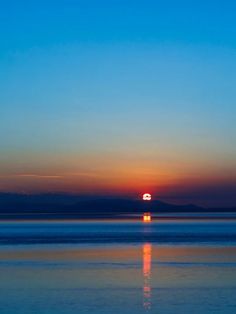 the sun is setting over the ocean with mountains in the distance and blue sky above