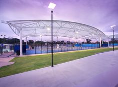 an empty tennis court is lit up at night with the lights on and green grass