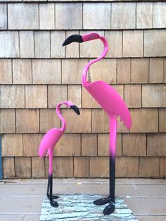 two pink flamingos standing next to each other in front of a brick wall,