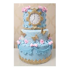 a three tiered blue cake with pink flowers and butterflies on it's side