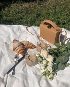 a table topped with flowers and food on top of a white cloth next to a brown bag