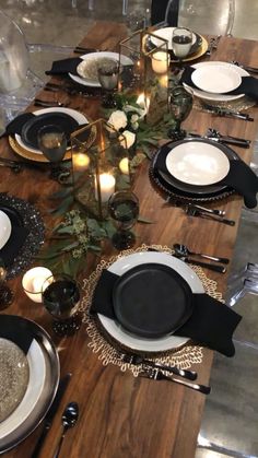 the table is set with black and white plates, silverware, candles and greenery