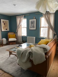 a living room filled with furniture and windows covered in white drapes on top of blue walls