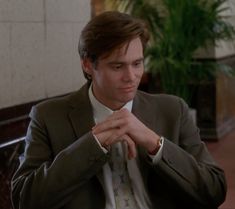 a man in a suit and tie sitting at a table with his hand on his chest