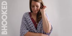 a woman wearing a crocheted shawl is holding her hair in one hand