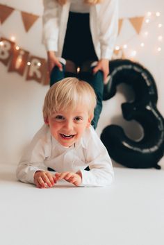 a little boy laying on the floor in front of a number 3 sign and smiling