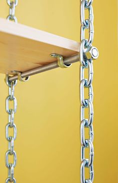 a wooden shelf with chains hanging from it's sides and a yellow wall in the background