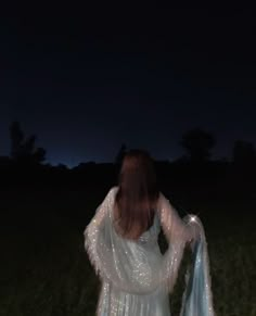 a woman standing in the grass at night wearing a white dress with sequins on it