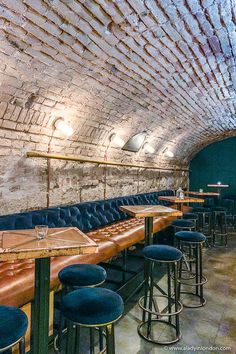 a long row of blue leather seats in a brick walled room with bar stools