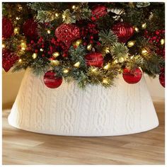 a white christmas tree skirt with red ornaments and lights on the top is sitting on a wooden floor