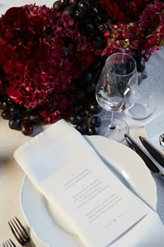 the table is set with white plates, silverware and red flowers in vases