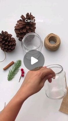 someone is holding a glass with pine cones and twine on the table next to it