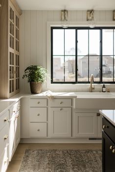 a kitchen with white cabinets and an area rug in front of the window that has a potted plant on it