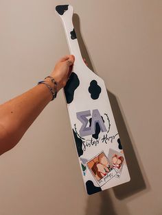 a person holding a wooden spatula shaped like a cow with pictures on it's side