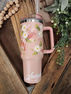 a pink coffee cup with flowers painted on it and the word loved next to it