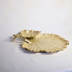 two gold leaf shaped dishes on a white surface