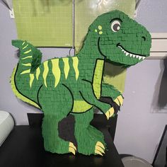 a paper model of a green dinosaur on a black table in front of a wall