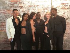 a group of people standing next to each other in front of a brick wall wearing black outfits