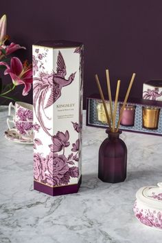 an assortment of candles and boxes on a marble table with orchids in the background