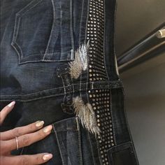 a woman's hand on the side of her jean pants with holes and rivets