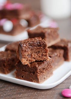 chocolate brownies stacked on top of each other on a white plate next to pink and white candy