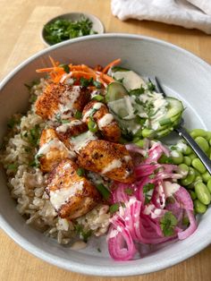 a bowl filled with rice, meat and veggies on top of a wooden table