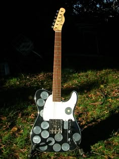 a black and white guitar with polka dots on it's body sitting in the grass