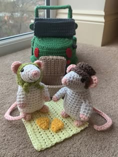 two crocheted mice sitting next to each other on top of a rug in front of a window