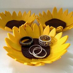 two sunflower shaped trays with wedding rings on them and one ring holder in the middle