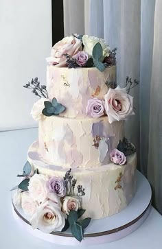 a three tiered wedding cake with pink flowers on the side and greenery around it