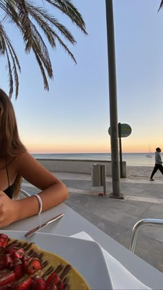 a woman sitting at a table in front of a plate of food on the beach