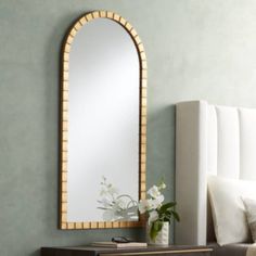 a mirror sitting on top of a wooden dresser next to a vase with flowers in it