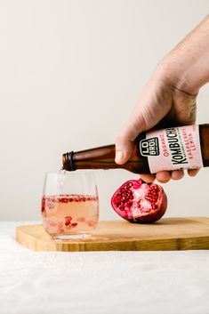 a person pouring pomegranate into a glass on a cutting board next to a bottle