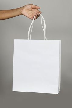 a person's hand holding a white shopping bag against a gray background with copy space