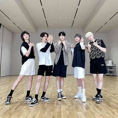 four young men standing on top of a wooden floor in front of a white wall