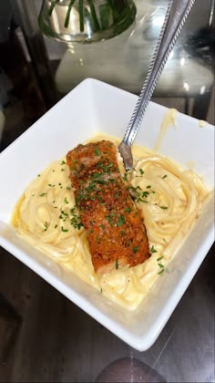 a square white plate topped with pasta and meat covered in parmesan cheese sauce