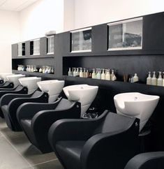 a row of black and white sinks in a room with pictures on the wall behind them