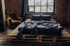 a bed made out of wooden pallets in front of a brick wall and window