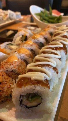 sushi rolls are lined up on a long white plate with sauce drizzled over them