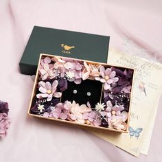 a box that has some flowers inside of it on a pink surface next to purple flowers