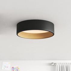 a black circular light fixture hanging from the ceiling in a room with white walls and curtains