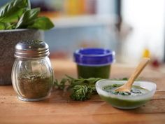 a wooden table topped with two jars filled with green liquid and herbs next to each other