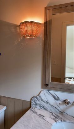 a bathroom with a marble counter top and white sink under a light fixture on the wall