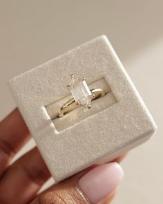 a woman's hand holding an engagement ring in a white box with a diamond on it