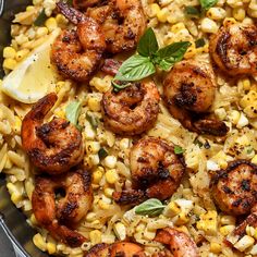 a skillet filled with shrimp, corn and basil garnished with lemon wedges