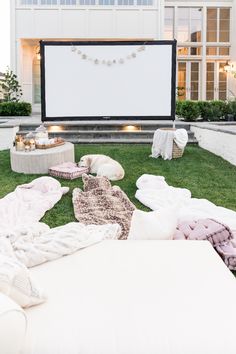 an outdoor movie is set up on the lawn with blankets, pillows and lights around it