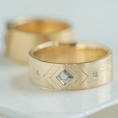 two wedding rings sitting on top of a white table next to each other with diamonds in them