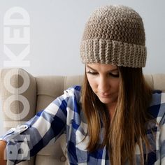 a woman sitting on a couch wearing a knitted hat and looking at her cell phone