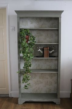 an old bookcase with ivy growing on top and books in the bottom, along with two deer heads